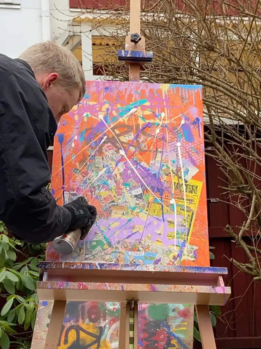 Andreas holding a spray can making a colourful pop art painting on a canvas.
