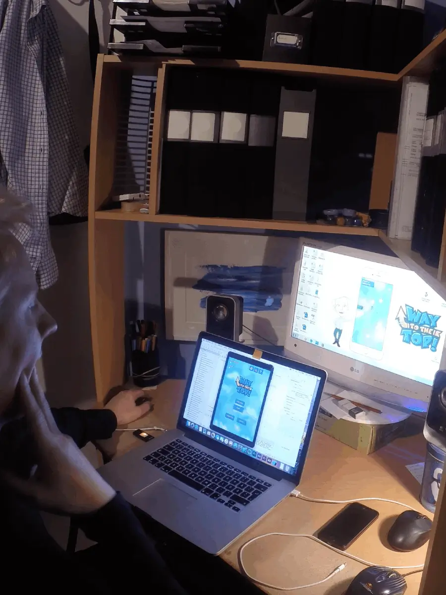 Andreas Falk infront of two computer screens and an iPhone making the mobile game Way to the top