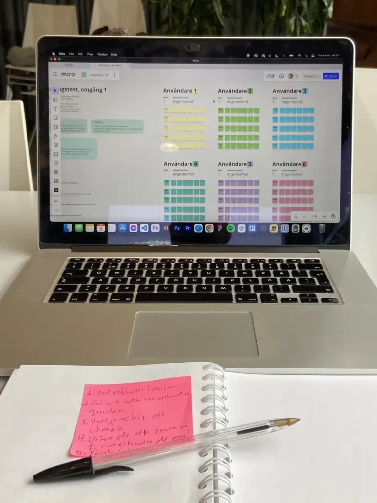 Pen and paper with a computer showcasing a set up in Miro to take notes during usability tests